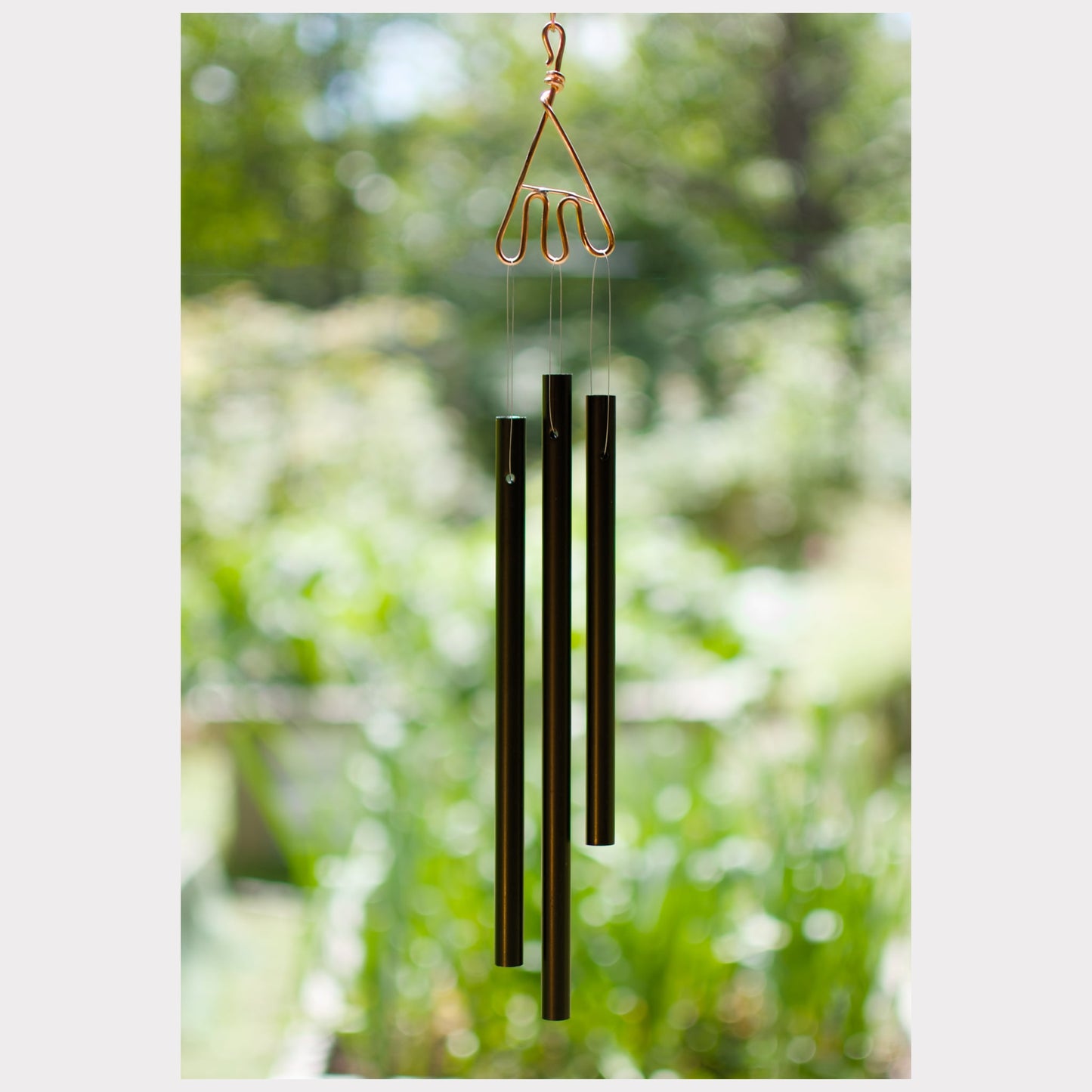 Decorative wind chime with three cylindrical metal components against a blurred green outdoor background