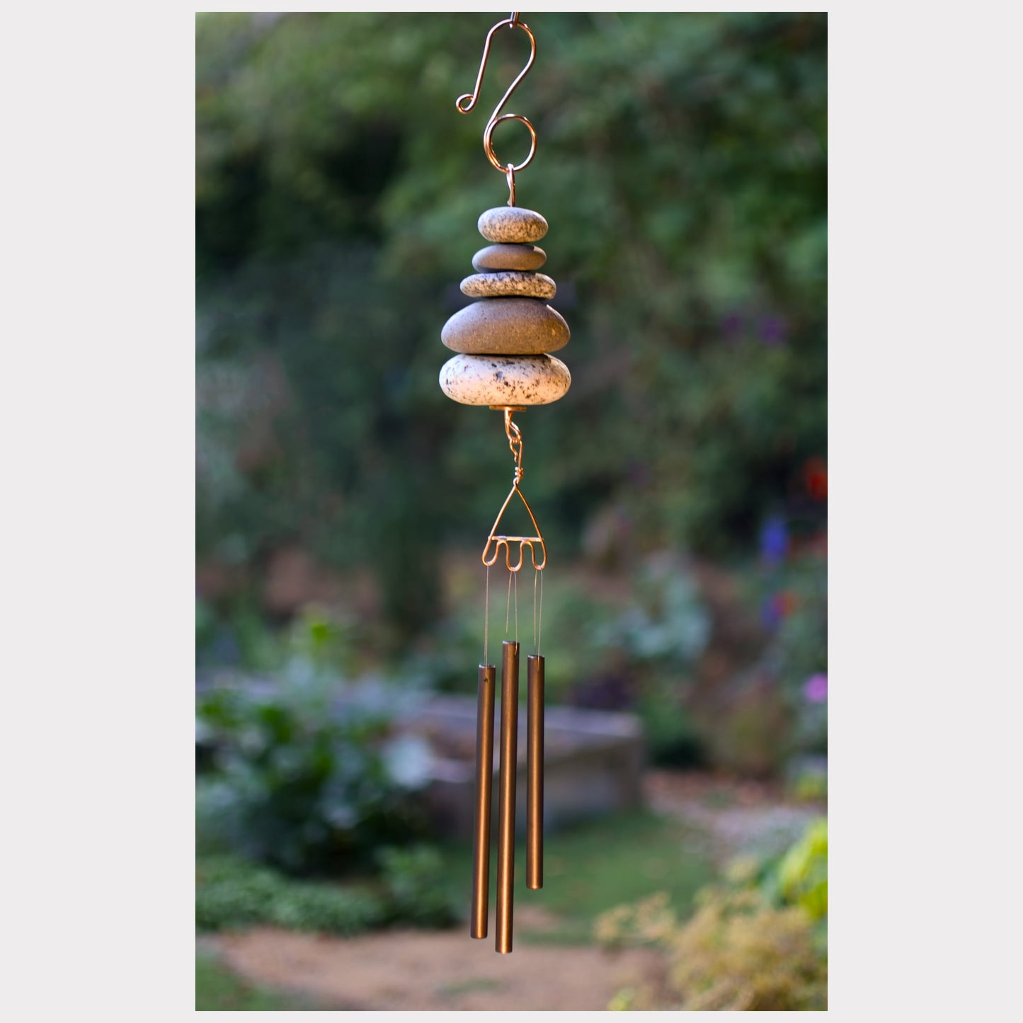 Decorative wind chime with stones and metal tubes against a garden background