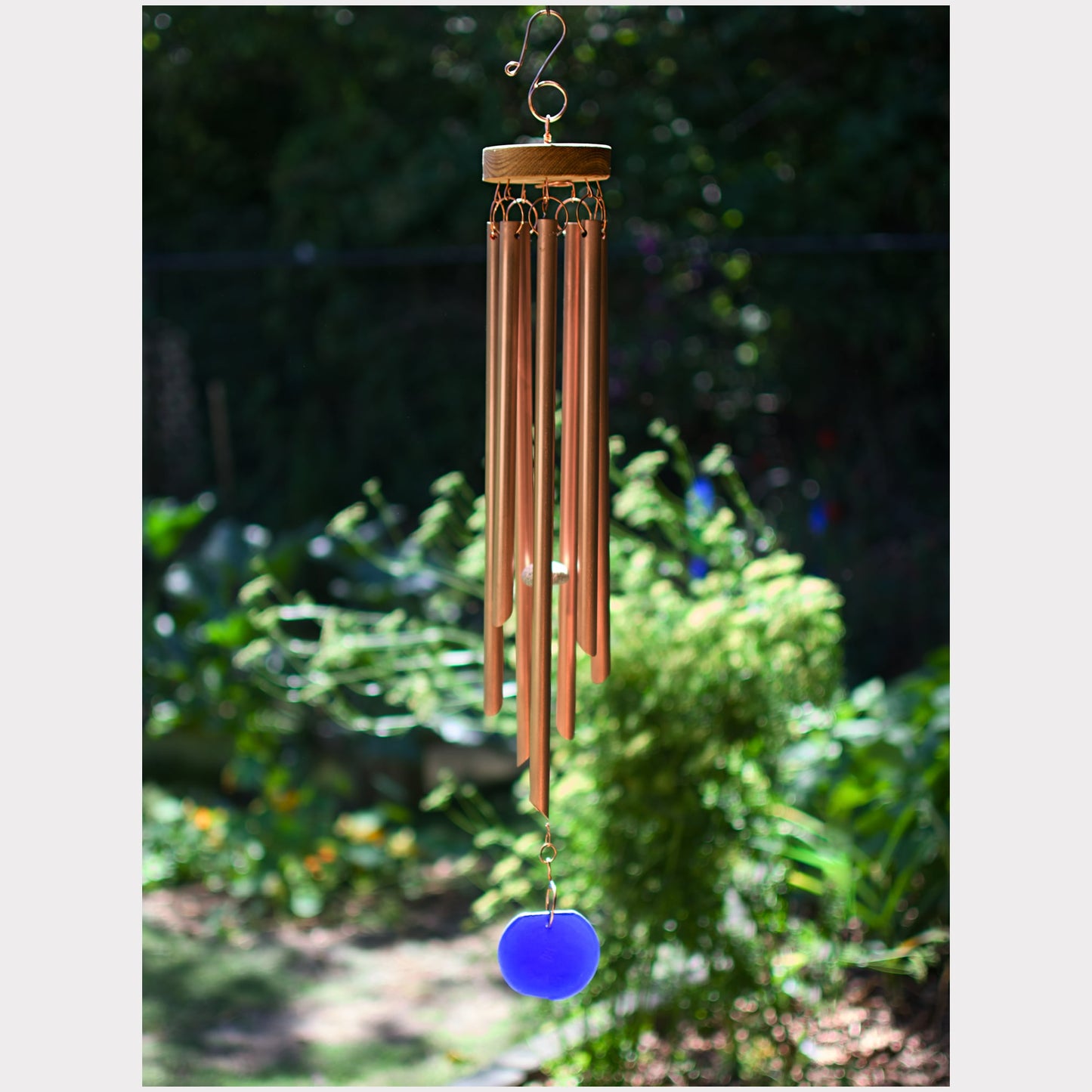 Copper wind chime with a blue accent hanging in a garden
