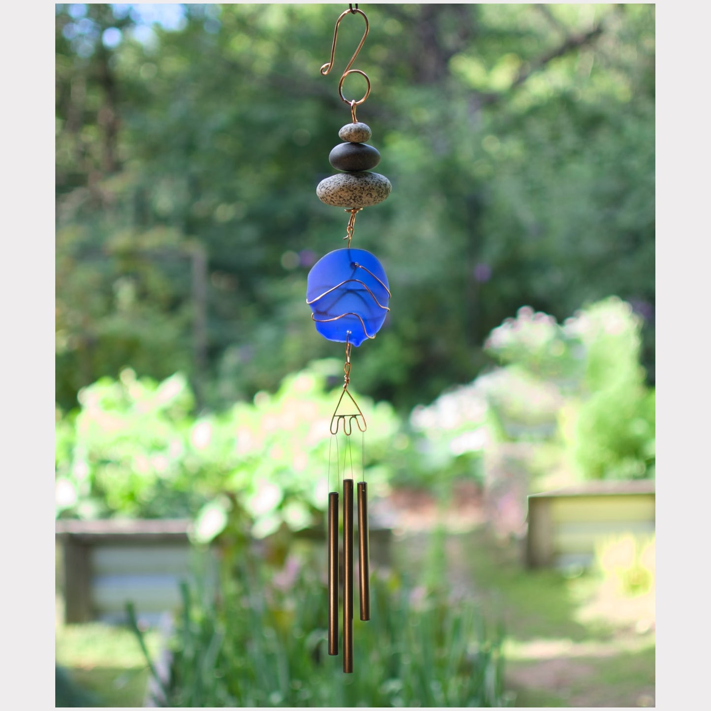Decorative wind chime with blue glass and brass elements against a blurred garden background