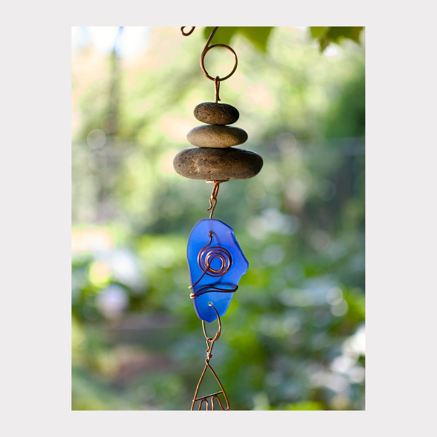 Decorative hanging with blue glass piece and stones against a blurred green background