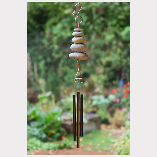 Decorative wind chime with stacked stones and metal components against a garden background