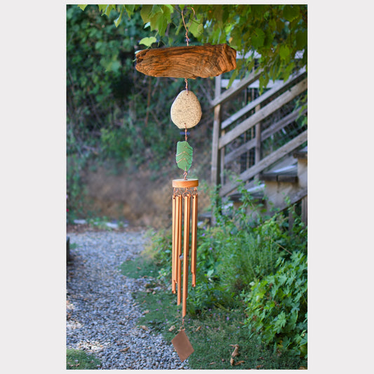 Driftwood wind chime hanging outdoors with greenery in the background.