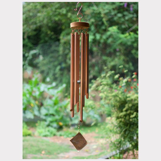 Copper wind chime hanging against a blurred green garden background