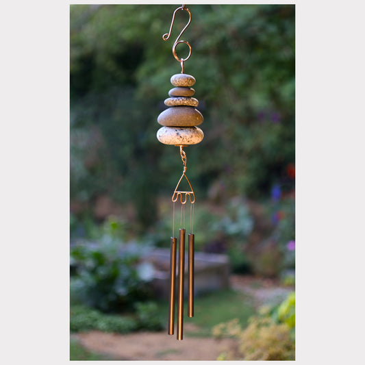 Decorative wind chime with stones and metal tubes against a garden background