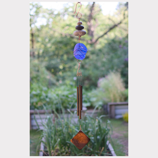 Decorative wind chime with blue and brown elements against a garden background