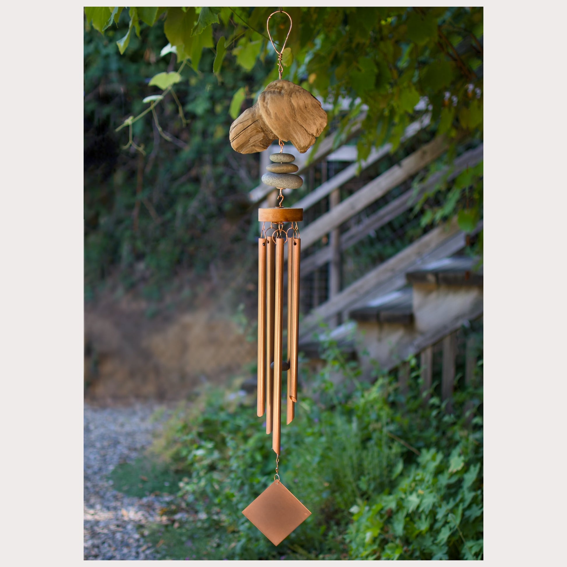 Decorative wind chime hanging outdoors with greenery in the background
