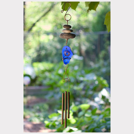 Decorative wind chime with blue glass piece and pebbles against a blurred green outdoor background